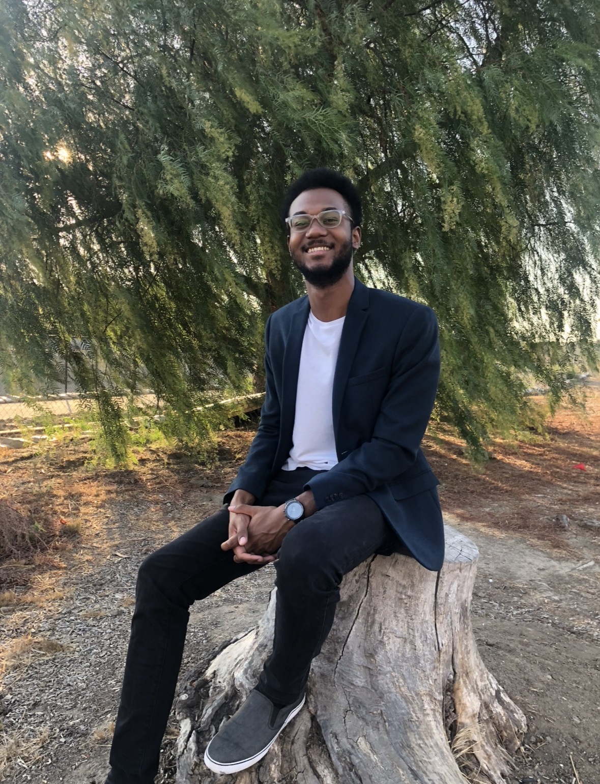 Chris Mukiibi, founder of BrightStar Education, seated outdoors under a willow tree